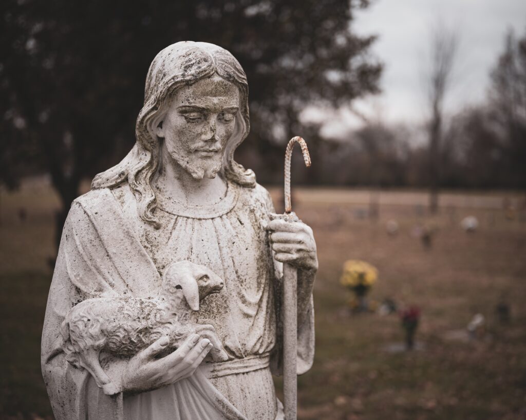 All Saints and All Souls Day 1 weathered statue jesus christ with sheep his hands blurred background